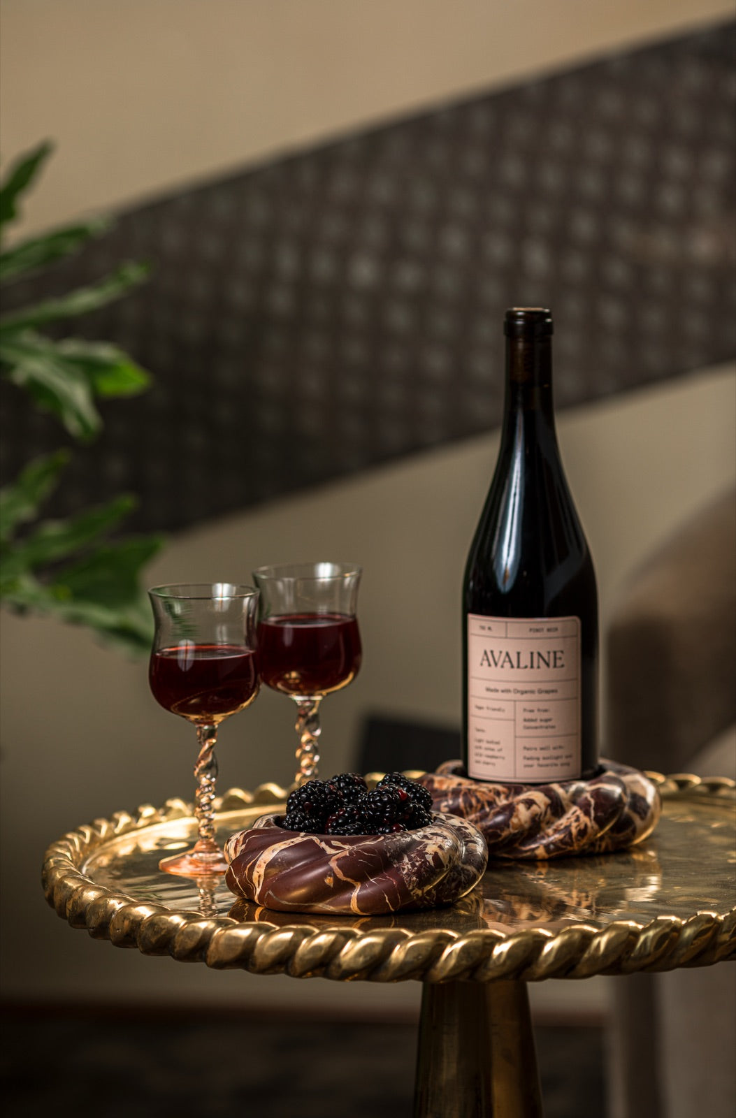 Wine Coaster in Cabernet Red Marble holding a bottle of Avaline red wine beside a coaster of blackberries and two glasses of red wine on a brass table