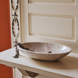 A travertine bowl on a white console against a terracotta wall