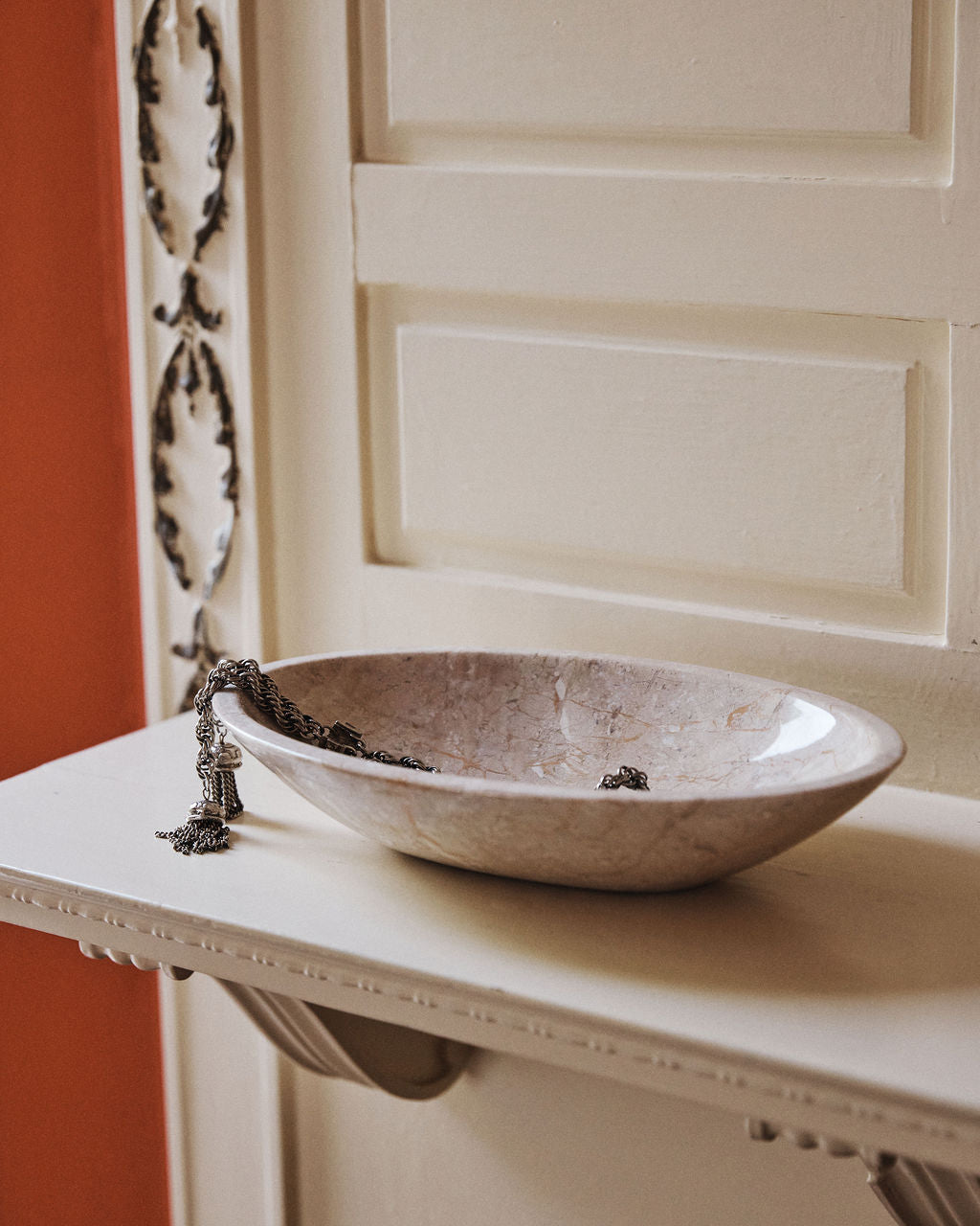 A travertine bowl on a white console against a terracotta wall