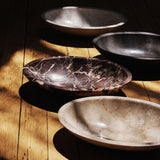 Three carved stone objects in travertine and burgundy marble grouped in raking sunlight