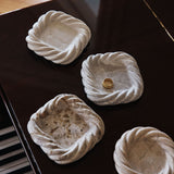 Five pale stone catchalls with twisted rims, seen from above on a black lacquered surface