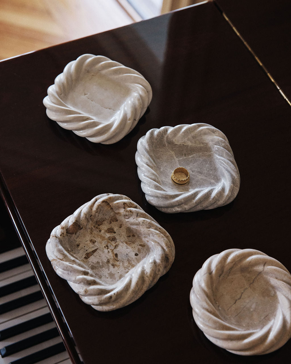 Five pale stone catchalls with twisted rims, seen from above on a black lacquered surface