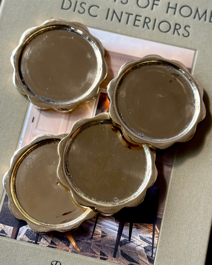 Sun Coaster Set in Brass, four scalloped brass coasters on a book