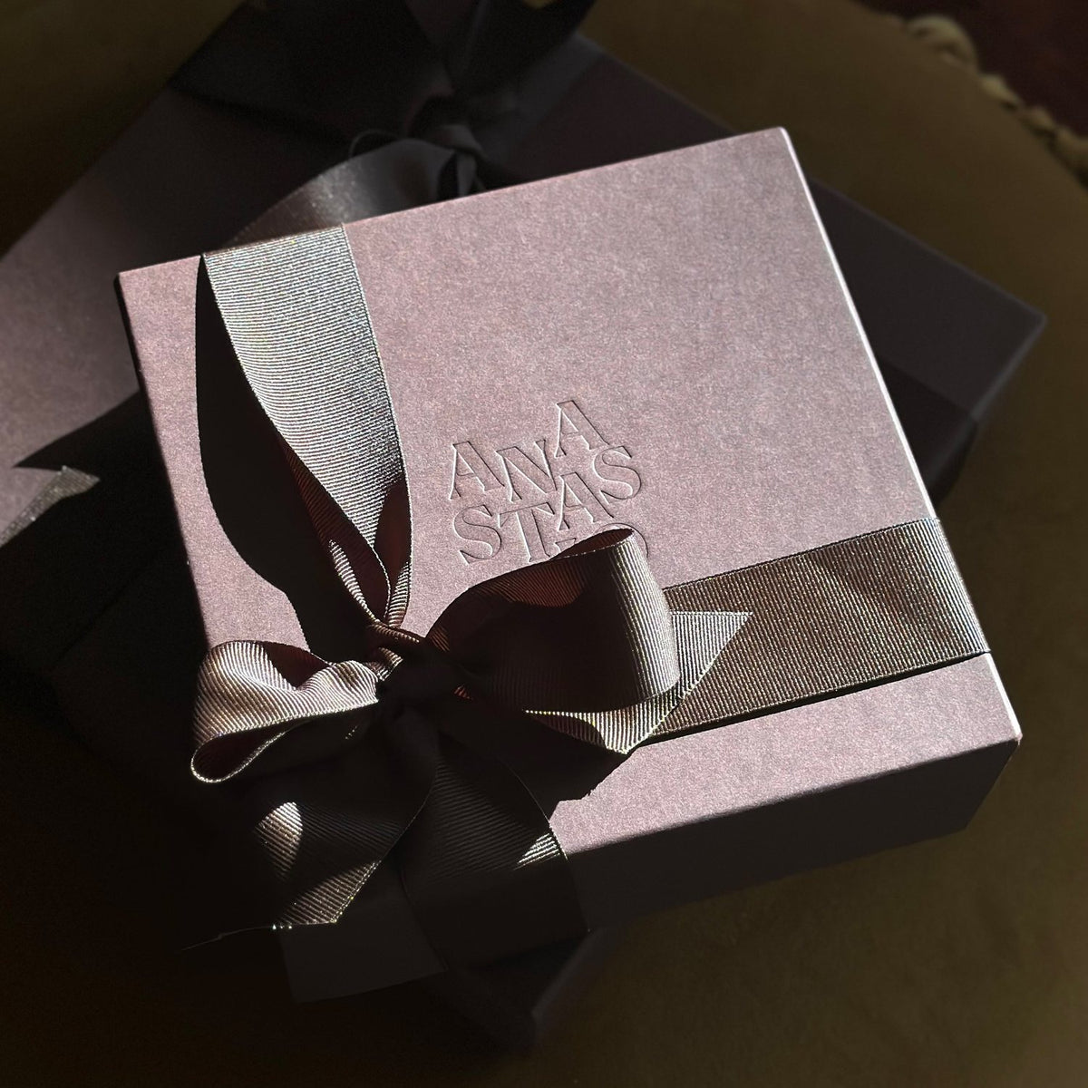 A mauve gift box embossed with the Anastasio name, tied with a taupe ribbon