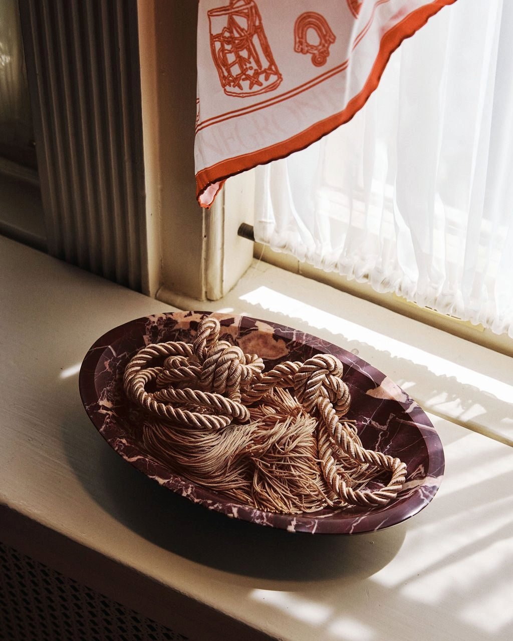 Isla Bowl in Cherry Gold marble holding a coiled cord on a sunlit windowsill
