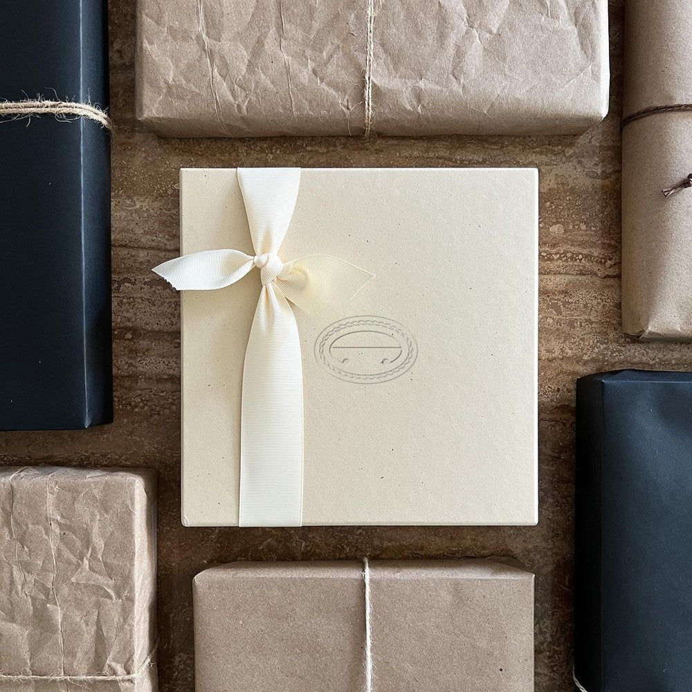 A cream gift box blind-debossed with the Anastasio Home rope emblem, tied with an ivory ribbon