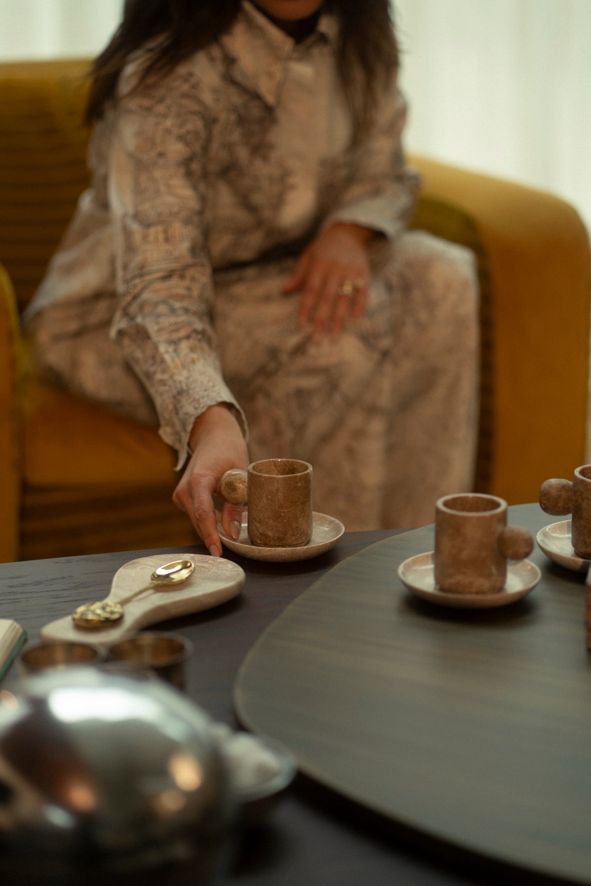 Tania Sarin in a citron armchair setting a marble cup on the table