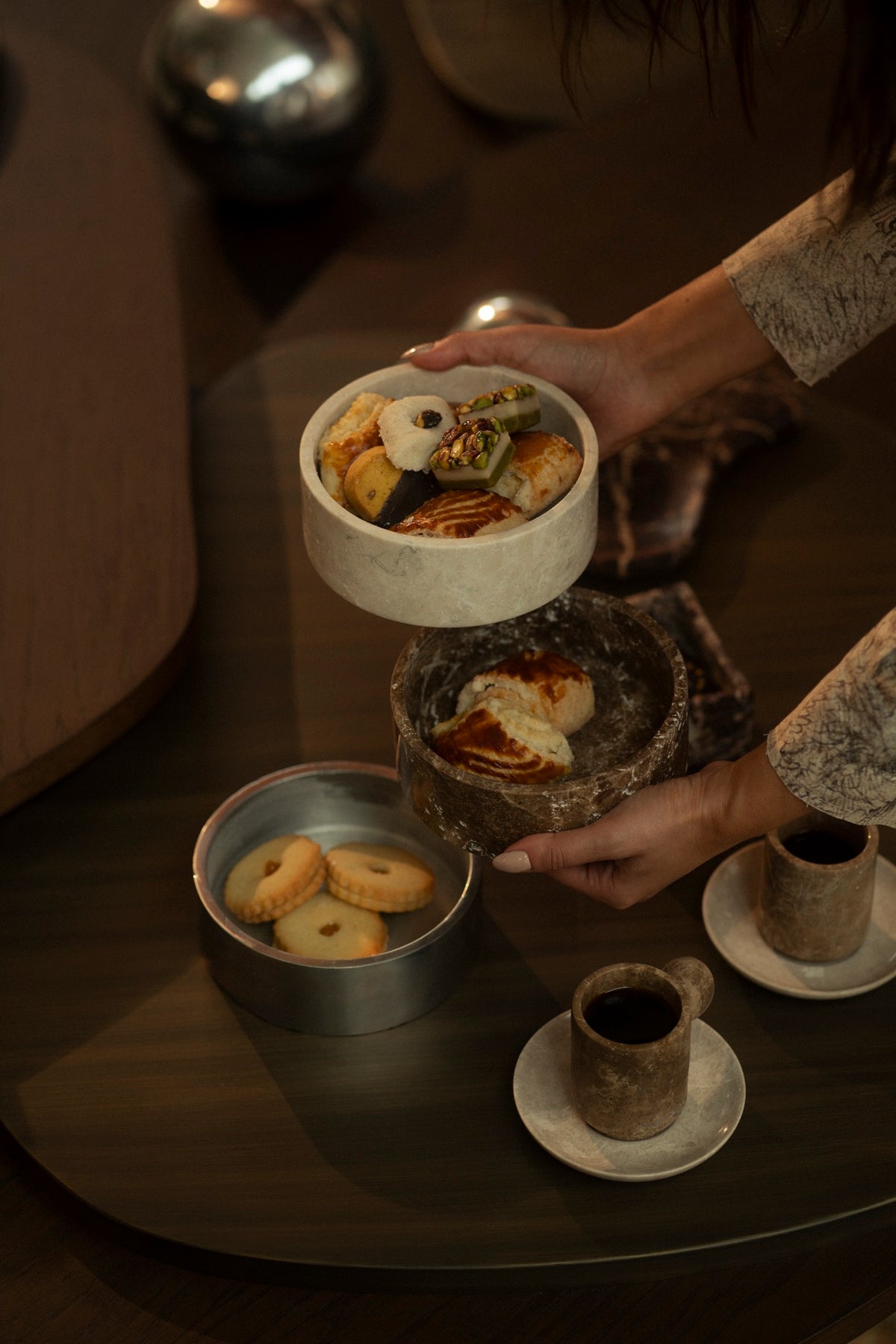 Hands lifting marble bowls of pastries from a dark wood table