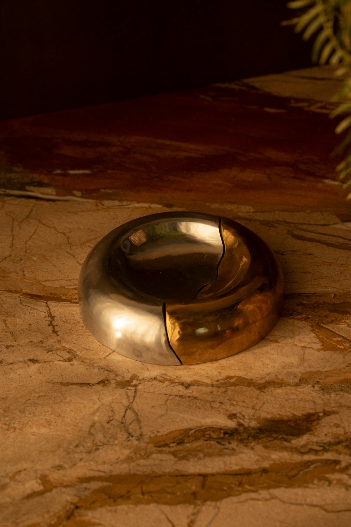 A brass and aluminum bowl on a marble counter in low light