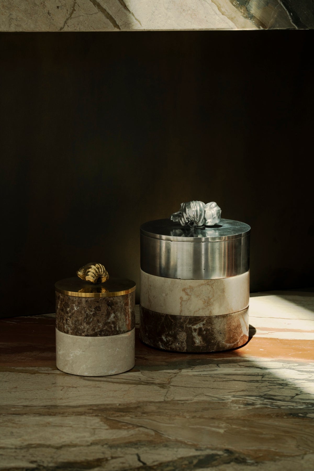 Stacked stone boxes with aluminum and brass lids on marble