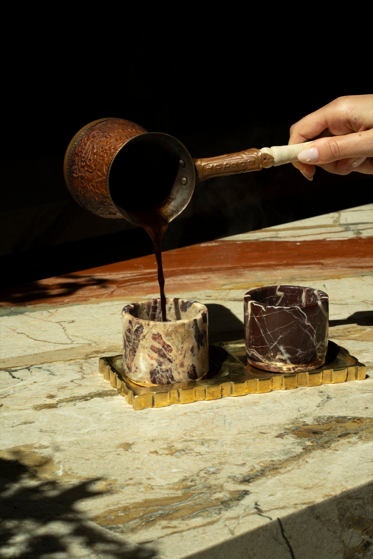 Coffee poured from a copper pot into Cherry Gold marble cups on a scalloped brass tray, on Tania's marble bar