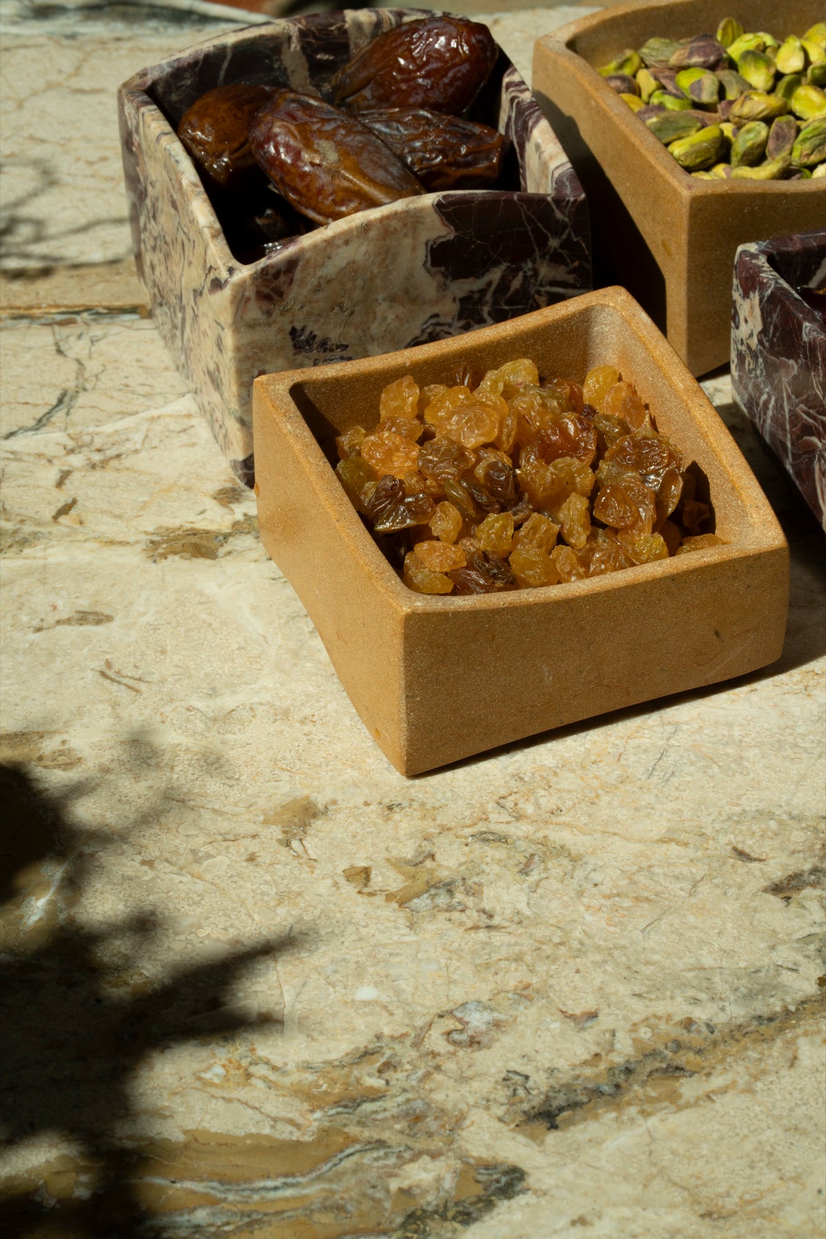 A stone box of golden raisins beside a marble box of dates
