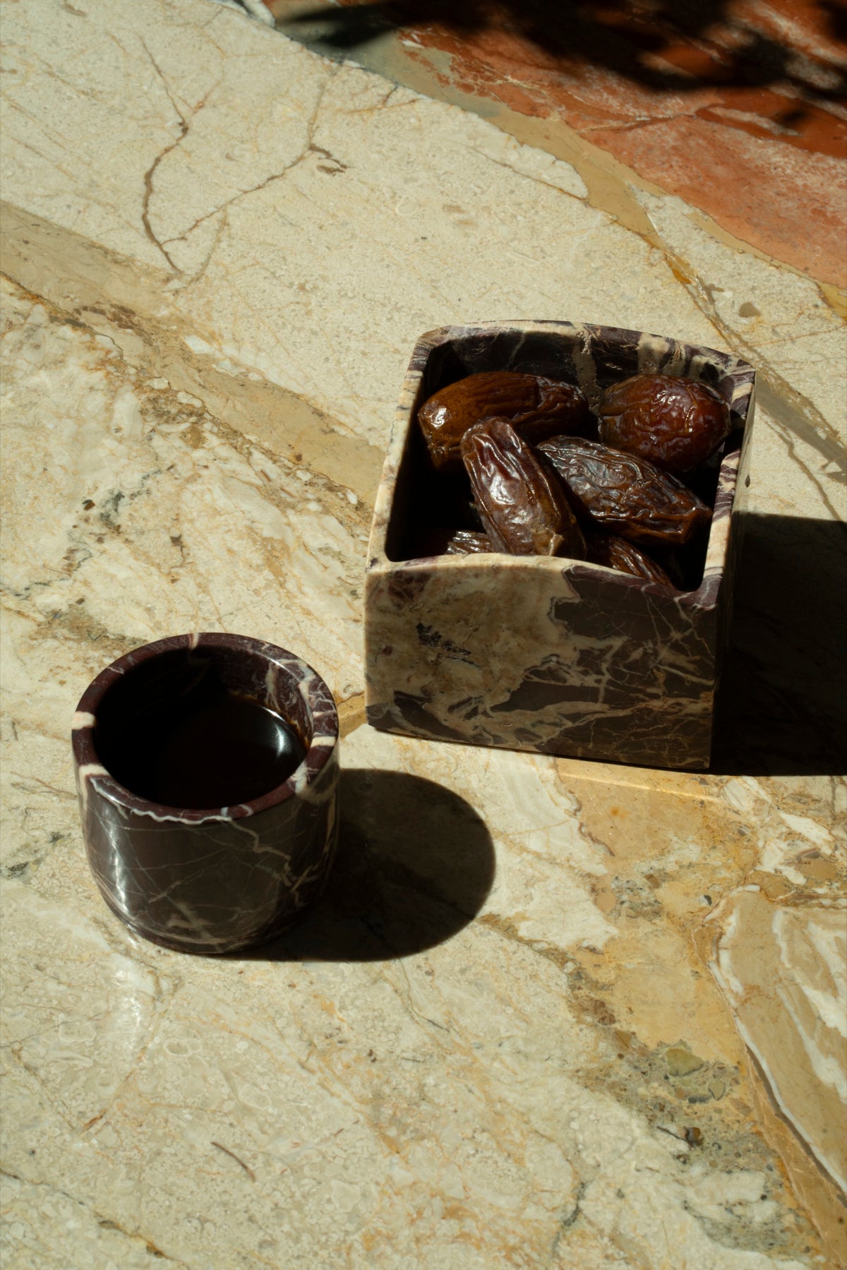 A marble box of dates beside a marble cup of coffee