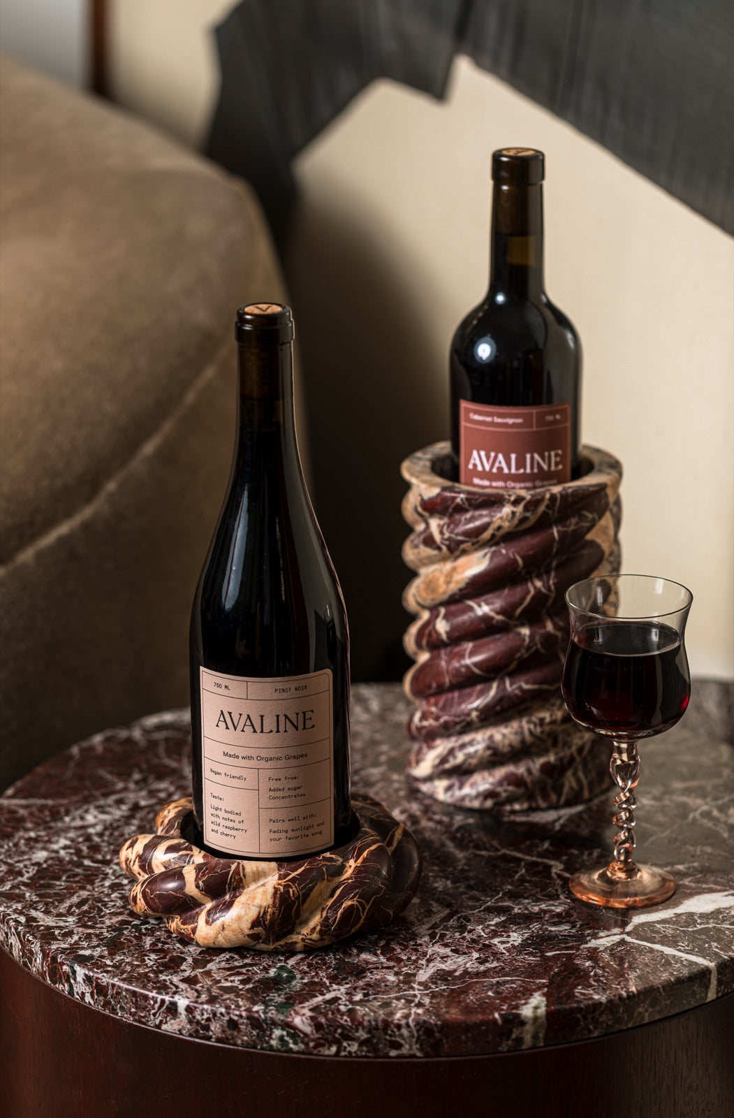 Wine Chiller and Wine Coaster in Cabernet Red Marble holding bottles of Avaline red wine on a red marble side table, with a glass of red wine