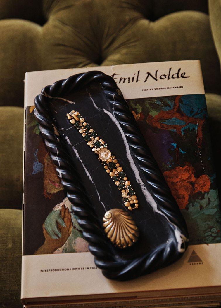 The Natalie Tray in a black marble with white veining, holding a gold watch and a gold shell, on a book