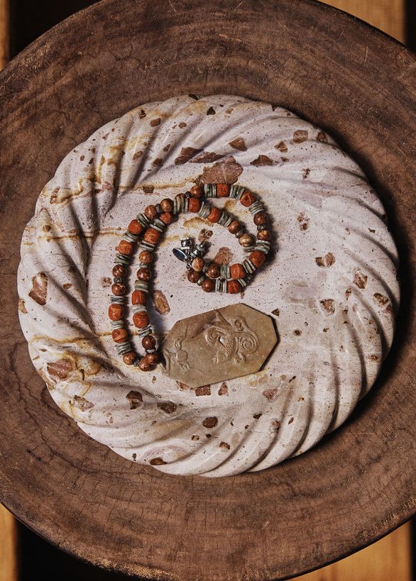 The Jordana Catch in a cream stone flecked with rust, holding a beaded necklace, in a carved wooden bowl