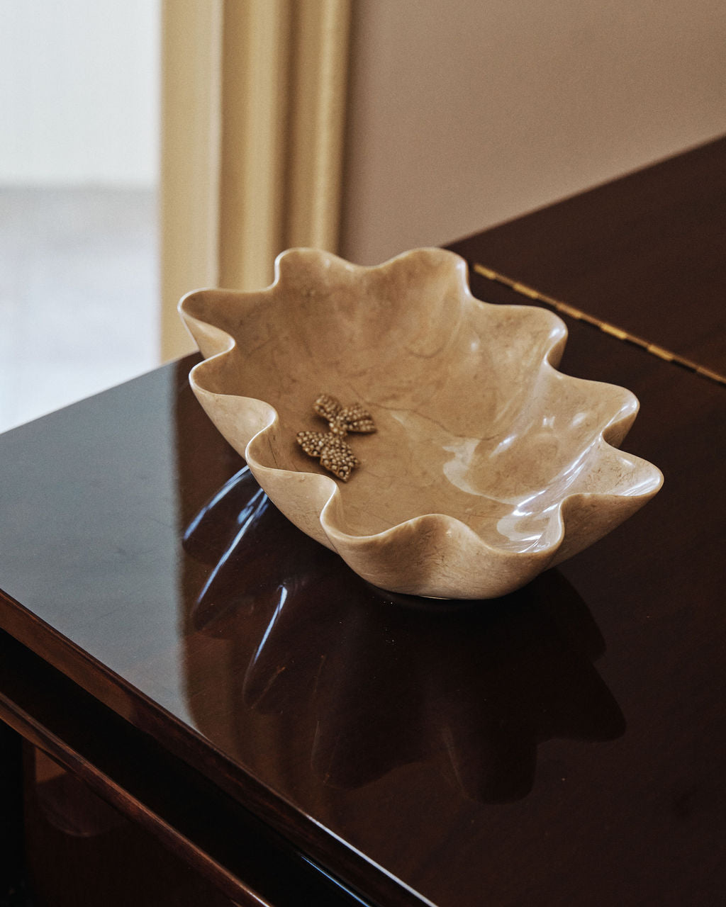 A large fluted cream stone bowl on a dark wood console